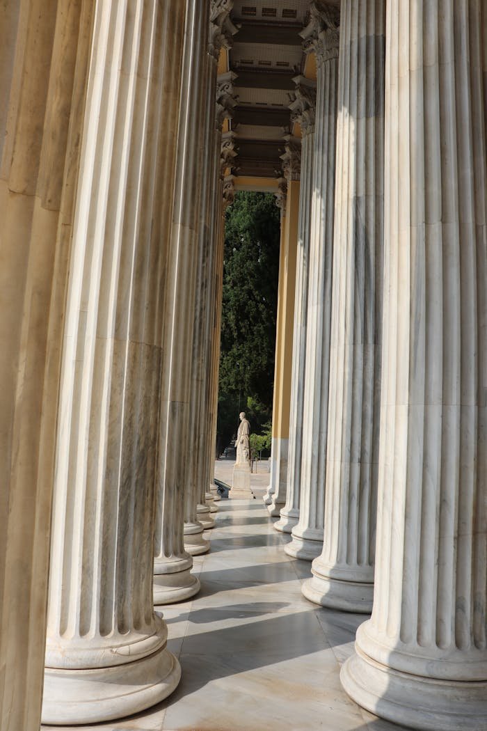 Elegant neoclassical marble columns with a distant statue in view, evoking ancient architectural grandeur.